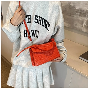 Detail of bright orange handbag with crocodile texture and decorative knot strap