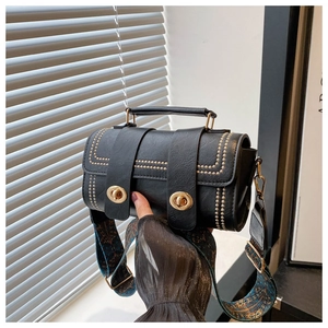 Vue détaillée d'un sac à main noir avec rivets dorés, fermoir rotatif et bandoulière brodée