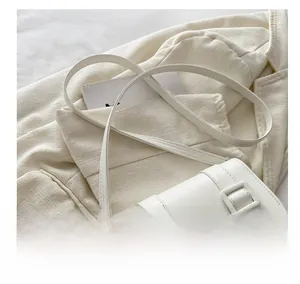 Detail view of a white leather saddle bag with square buckle on a creamy background