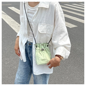 Close-up of light green drawstring bucket bag with black strap and metallic buckles