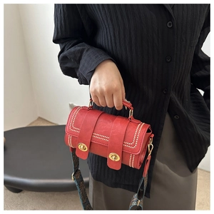 Detail of red cylinder handbag featuring gold twist locks and ethnic woven shoulder strap