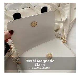 Detail view of the gold magnetic snap closure on a white leather saddle crossbody bag