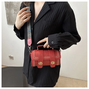 Detail of red cylinder bag with gold clasp and ethnic style embroidered shoulder strap