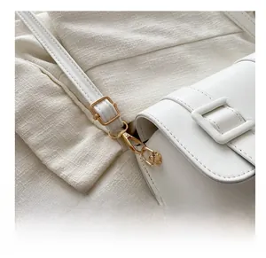 Close-up of golden metal hooks and adjustable strap on minimalist white saddle bag