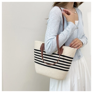 Detail of beige woven tote bag with black stripes and brown leather straps on model