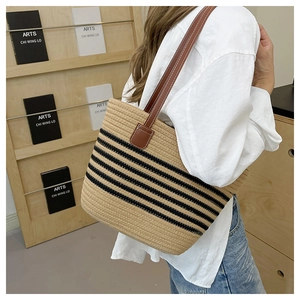 Detail of woven straw tote bag with black stripes and brown leather shoulder straps