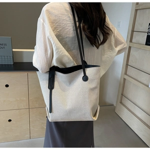 Close-up of a minimalist canvas tote bag with black leather straps on a model's shoulder