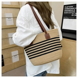Detail of woven straw tote bag featuring contrast black stripes and leather shoulder strap