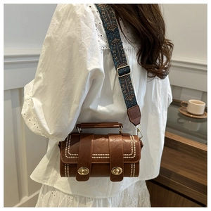 Gros plan du sac cylindre marron avec bandoulière bohème et détails dorés brillants