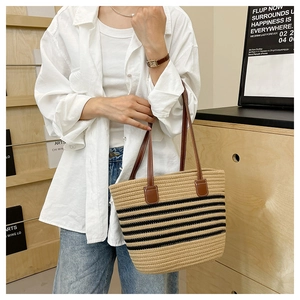 Close-up of woven straw tote bag featuring leather handles and black horizontal stripes
