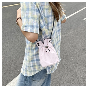 Detailed side view of a mini pink drawstring bucket bag with a slim black shoulder strap