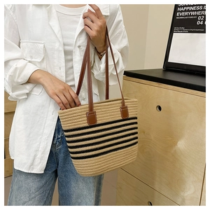 Close-up of woven straw tote bag featuring black stripes and brown leather handles