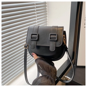 Detail of a black matte leather saddle bag with double buckle flap and gold hardware