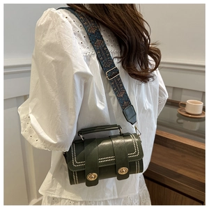 Detail of dark green cylindrical crossbody bag with woven bohemian strap and metal locks