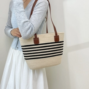 Large woven straw beach bag with black stripes and brown leather straps on model
