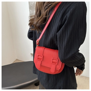 Detail of red leather crossbody bag with magnetic closure and decorative strap buckles