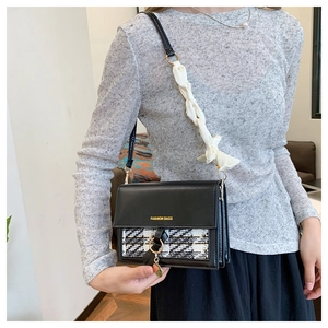 Detail of black crossbody bag with tweed flap, gold ring, and silk scarf handle
