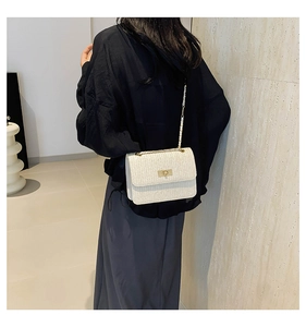 Detailed view of white woven shoulder bag with gold twist lock on a modern model