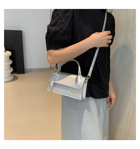 Sac bandoulière argenté brillant avec poignée fixe porté par un mannequin dans un décor épuré