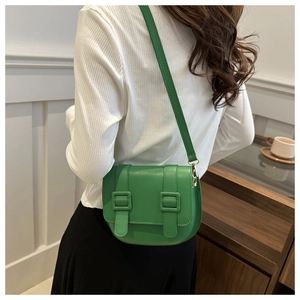 Model wearing a vibrant green saddle bag with faux leather texture and buckle straps