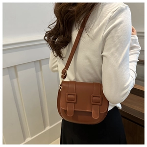 Detail of brown leather saddle bag featuring vintage buckles and adjustable shoulder strap