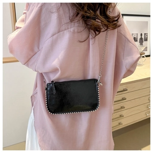 Détail d'un sac bandoulière en cuir verni noir avec perles argentées et chaîne
