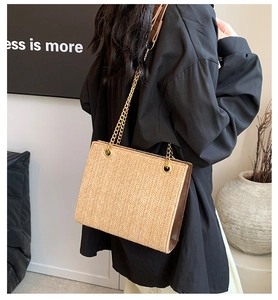 Detail of woven straw tote bag with brown leather side panels and gold chain strap
