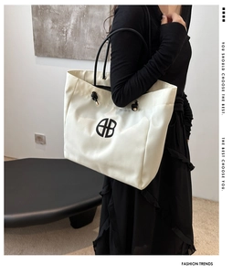Detail of ivory canvas tote bag with black handles and round geometric logo on a model