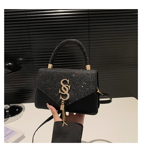 Detail of black glitter square bag with gold metal S logo and decorative tassel