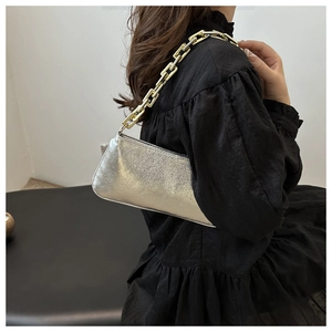 Detail of silver metallic handbag with thick gold chain strap worn with black dress