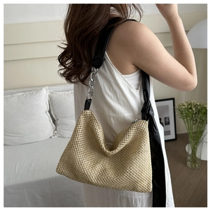 Detail of woven straw hobo bag with black ribbon knot and metal chain shoulder strap