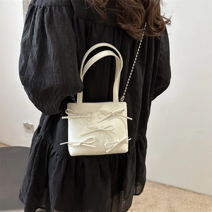 Minimalist white chain shoulder bag with 3D bow accents worn by a female model