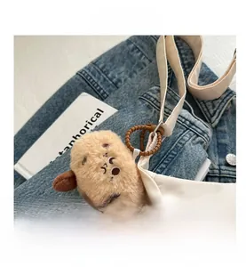 Detail of plush capybara charm hanging on a white nylon bag with denim background