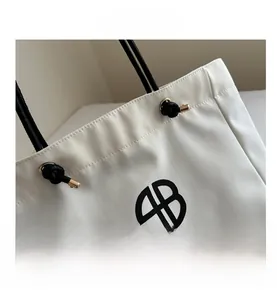 Close-up of white canvas tote bag with black drawstring detail and circular logo