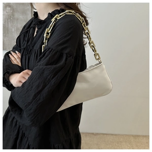 Detailed side view of a white baguette bag with a chunky gold chain strap on a model