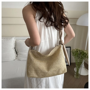 Detailed close-up of woven straw tote bag with elegant leather knot shoulder strap detail