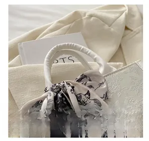 Detail of white jacquard tote bag featuring floral embroidery and printed silk scarf handle