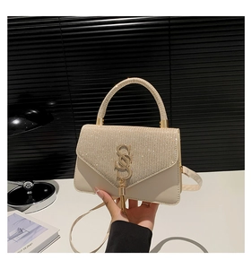 Detail of beige woven handbag featuring a metallic logo, fringe charm, and sparkling lid