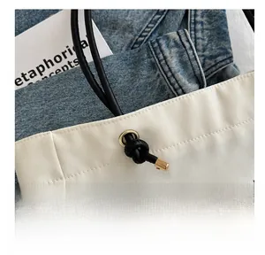 Close-up of white canvas tote bag featuring metal eyelets and black rope handle details