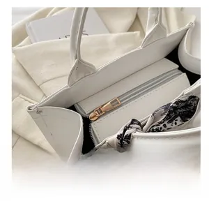 Detail of smooth golden zipper closure and elegant white tote bag with silk scarf handle
