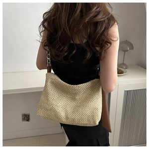 Detail of woven straw tote bag featuring brown leather strap and silver metal chain link