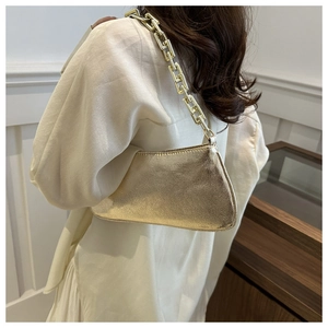 Close-up of a metallic gold underarm bag with a bold chain strap worn on the shoulder
