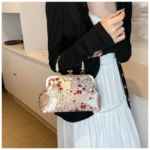 Detail of vintage floral embroidery on satin handbag with elegant gold metal clasp handle
