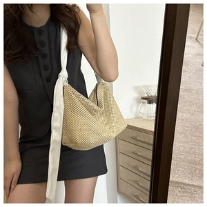 Detail of woven straw tote bag featuring decorative white ribbon knot wide shoulder strap
