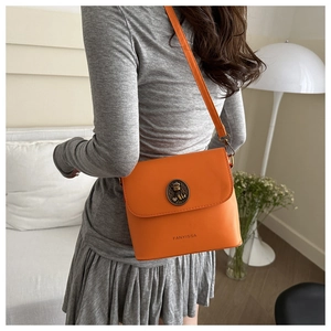 Detail of orange crossbody bag featuring a vintage gold cat relief buckle and FANYISSA logo