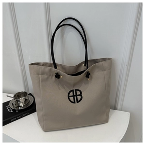 Detail of beige canvas tote bag showing the geometric logo and black drawstring handles