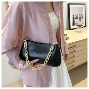 Detail of black baguette bag with chunky gold chain handle held by a model