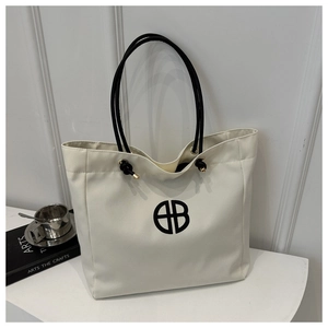 Detail shot of white canvas tote bag with black minimalist logo and golden metal accents