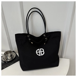 Close-up of black canvas tote bag with white circular logo and gold metal eyelet detail