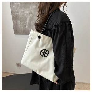 Detail of white canvas tote bag featuring black logo and rope shoulder straps